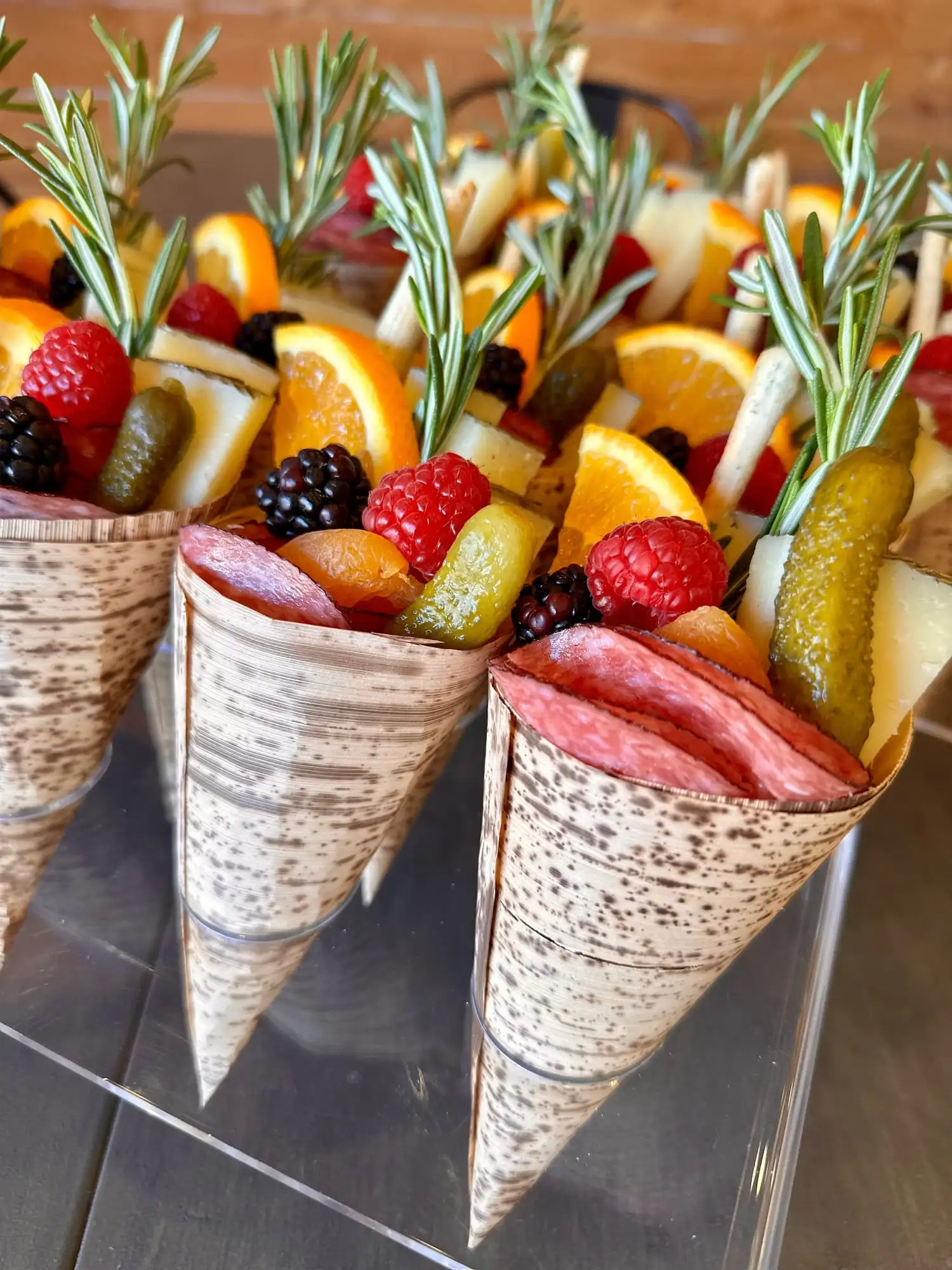 Row of charcuterie cones with cheese, salami, fruit and breadsticks in an acrylic stand (view 2)
