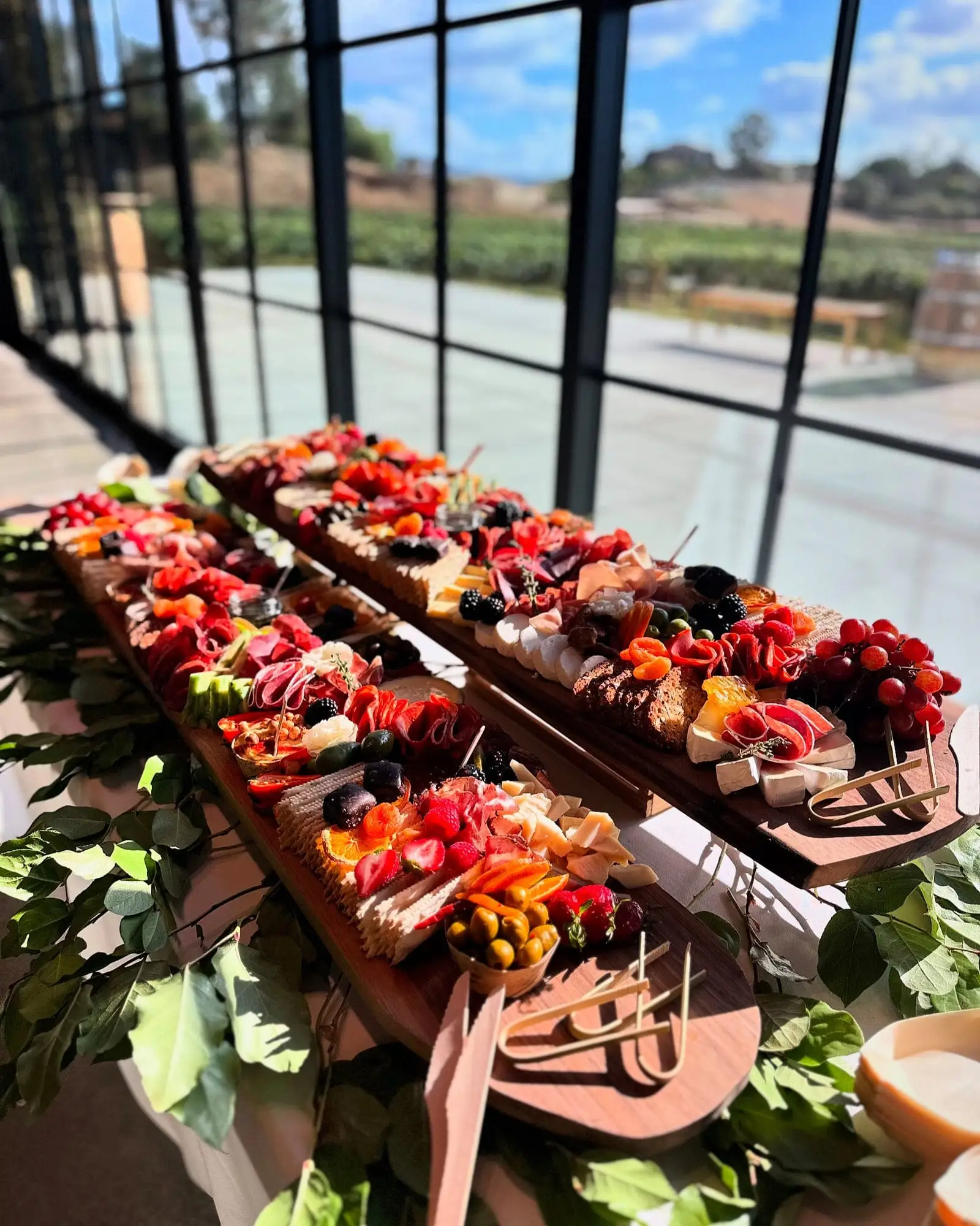 Two Boujee Boards of cheeses, cured meats and fruit on a table by tall windows overlooking Temecula vineyards